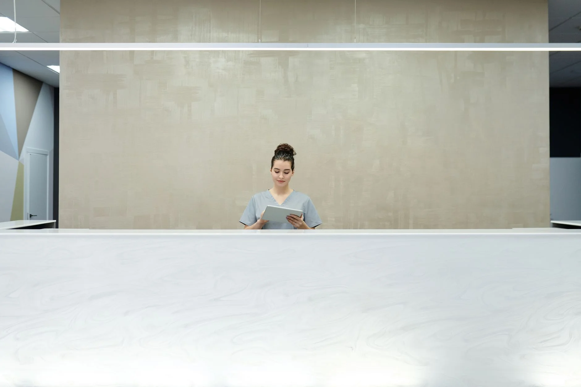 A woman receptionist using a tablet at a modern office reception desk.