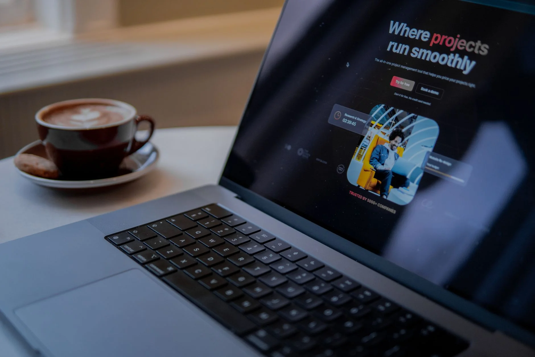 A laptop showing a project management board beside a cup of cappuccino.