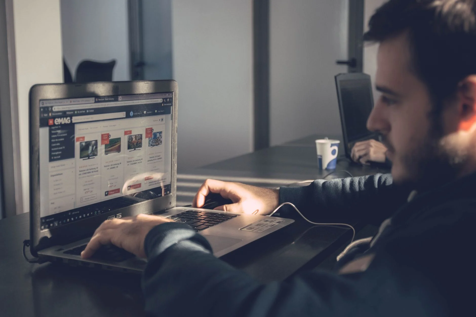 Adult man using laptop to browse an online marketplace in a modern office.