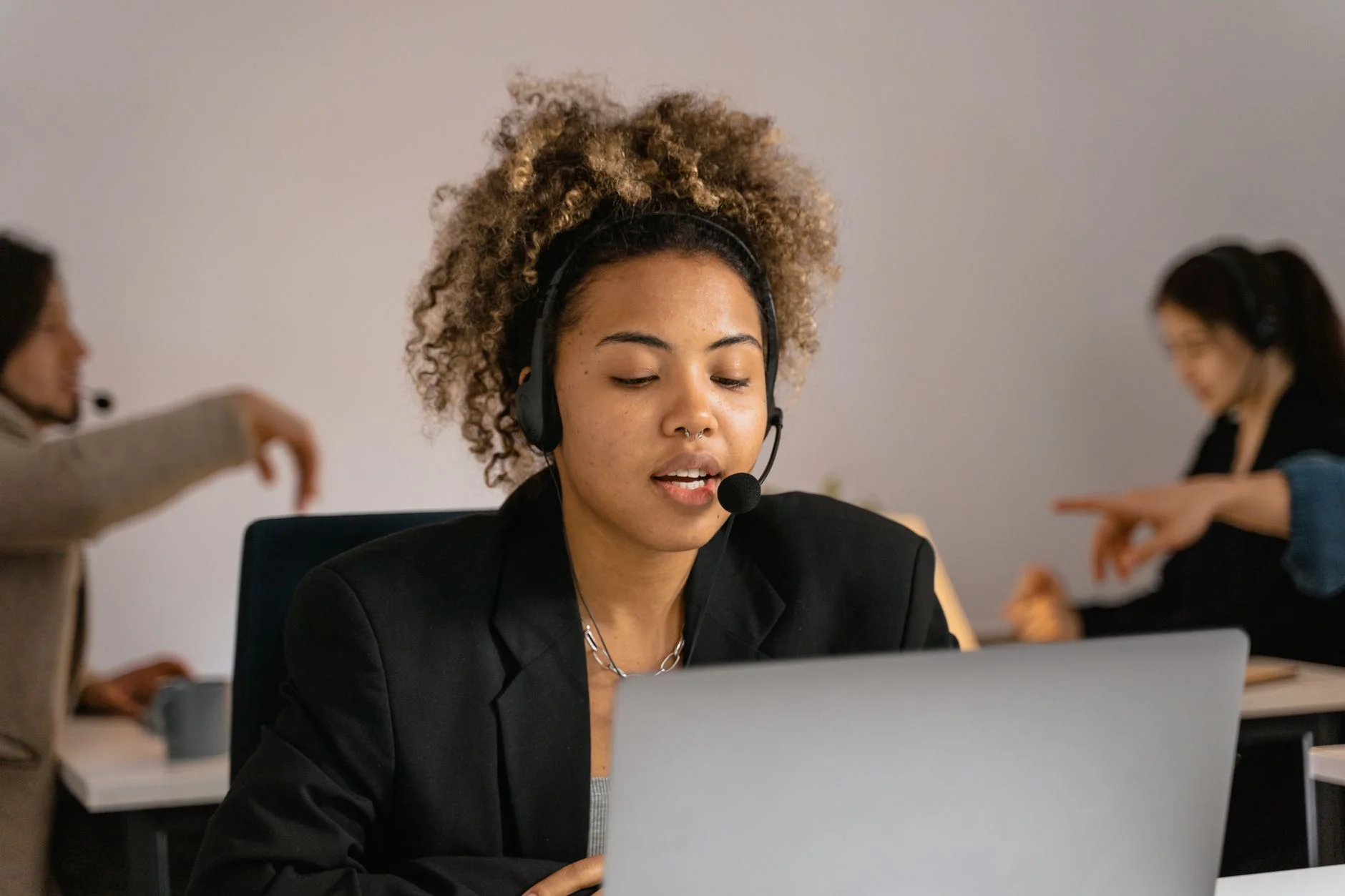 A professional wearing a headset works at a laptop in a bright office.